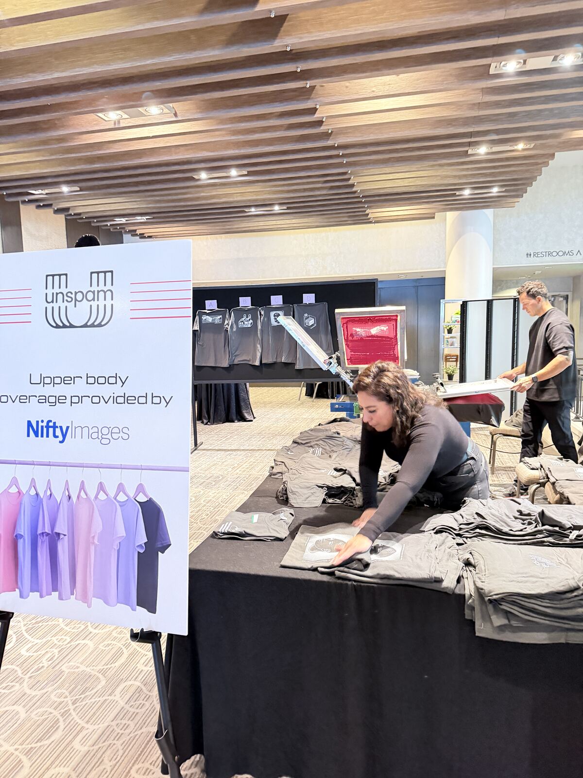 Person presenting at a corporate event with signage and merchandise booth setup in the background